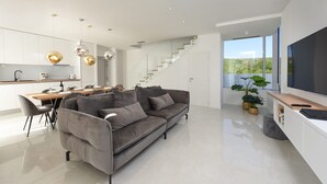 Ein zeitgemäßer Wohnraum mit grauem Sofa, einem Essbereich und einer Treppe, die auf einen Balkon mit Blick führt.