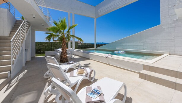 Ein moderner Außenbereich mit weißen Liegestühlen, einer Palme und einem Pool.