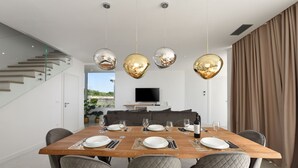 Ein modernes Esszimmer mit einem Holztisch, gedeckt für sechs Personen, einer Treppe links und einem Fernseher im Hintergrund.