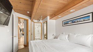 A bedroom with a large bed, wooden ceiling, a mounted TV, and a framed picture on the wall.
