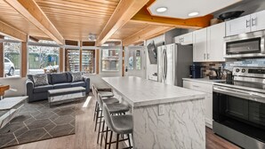 A modern kitchen with a marble island, stainless steel appliances, and a wooden ceiling.