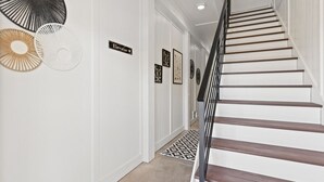 A staircase with a black handrail leading to an upper floor, white walls, and a patterned rug on the floor. - 1040 Break / 1040 Ocean Blvd West 4 Bedroom Home by RedAwning (Supply)
