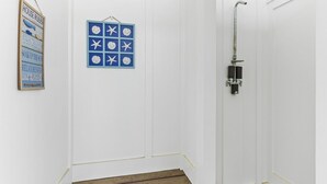 A white room with a wooden floor, a shower with a metal hose, and a blue sign with white stars and text. - 1040 Break / 1040 Ocean Blvd West 4 Bedroom Home by RedAwning (Supply)