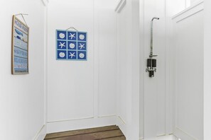 Ein heller Raum mit Holzboden, einer Dusche inklusive Duschschlauch und einem blauen Schild mit weißen Sternen und Schrift.