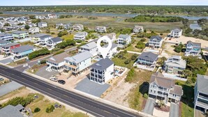 An aerial view of a coastal residential area with houses, a road, and a body of water in the background. - 1040 Break / 1040 Ocean Blvd West 4 Bedroom Home by RedAwning (Supply)