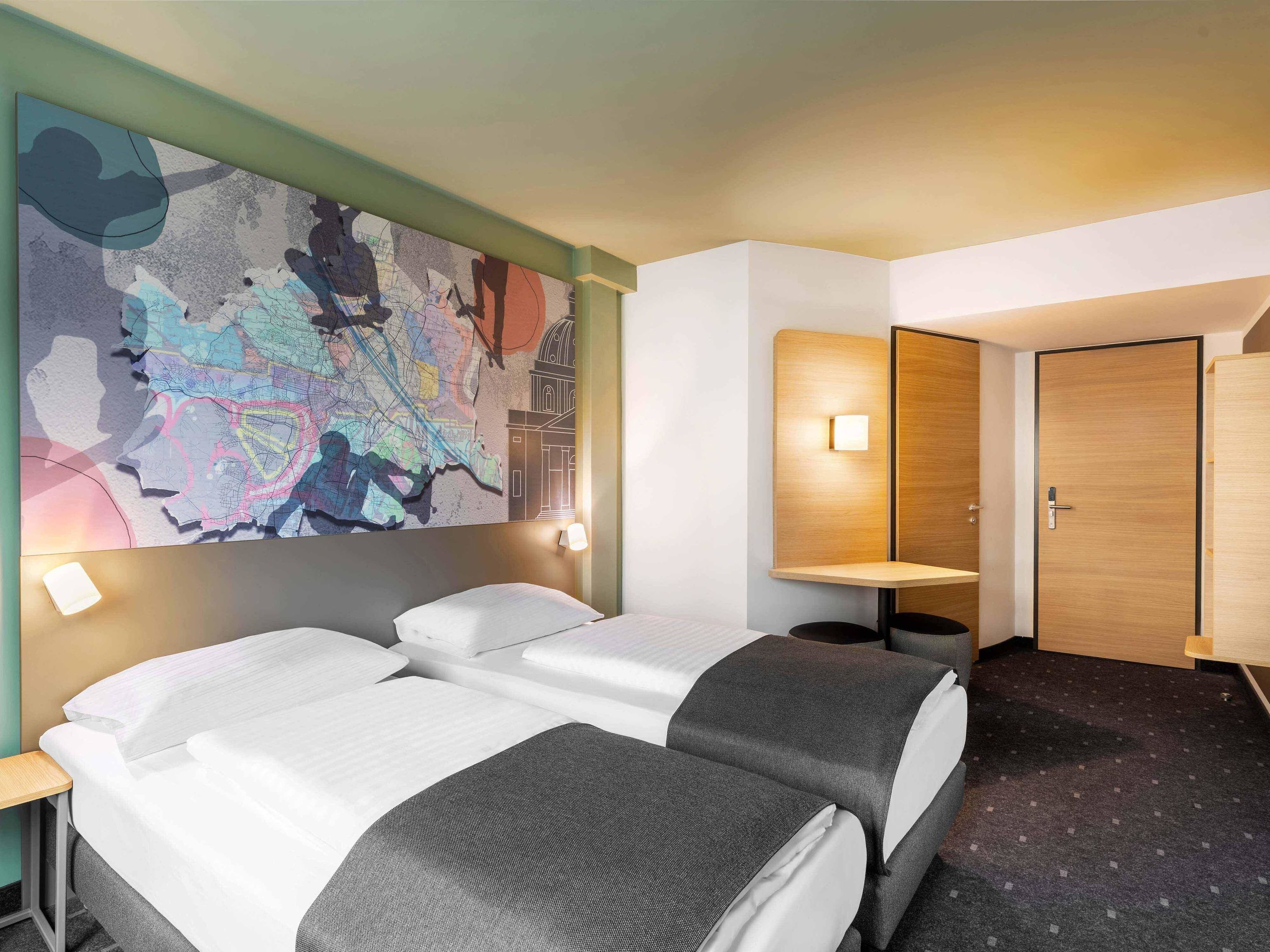 Ein Hotelzimmer mit zwei Betten, einer Wandmalerei mit einer Landkarte, einem Schreibtisch und einem Kleiderschrank.