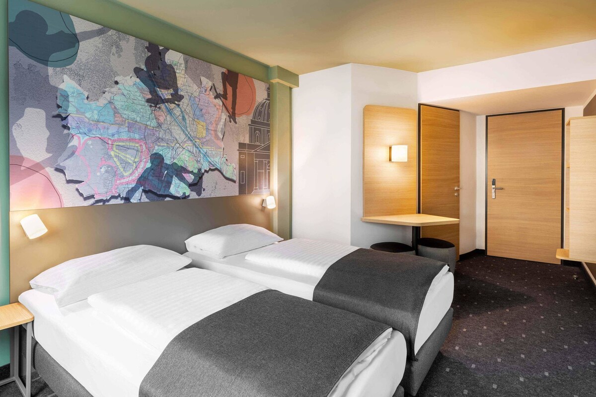 A hotel room with two beds, a map artwork on the wall, a desk, and a wardrobe.