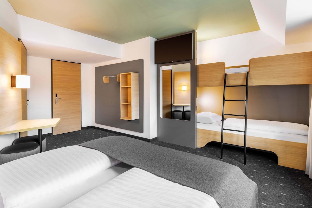 Una habitación de hotel moderna con literas, un escritorio, un armario y un espejo.