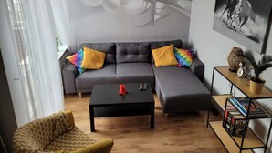 Una sala de estar moderna con un sofá seccional gris, una mesa de centro negra, un sillón amarillo y una estantería con libros y objetos decorativos.