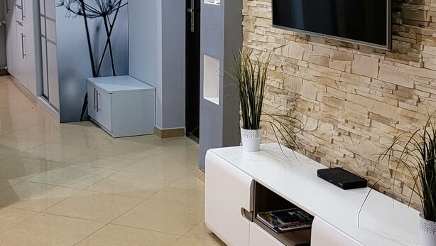 Una sala de estar moderna con una pared de piedra, un televisor montado y un mueble blanco para entretenimiento.