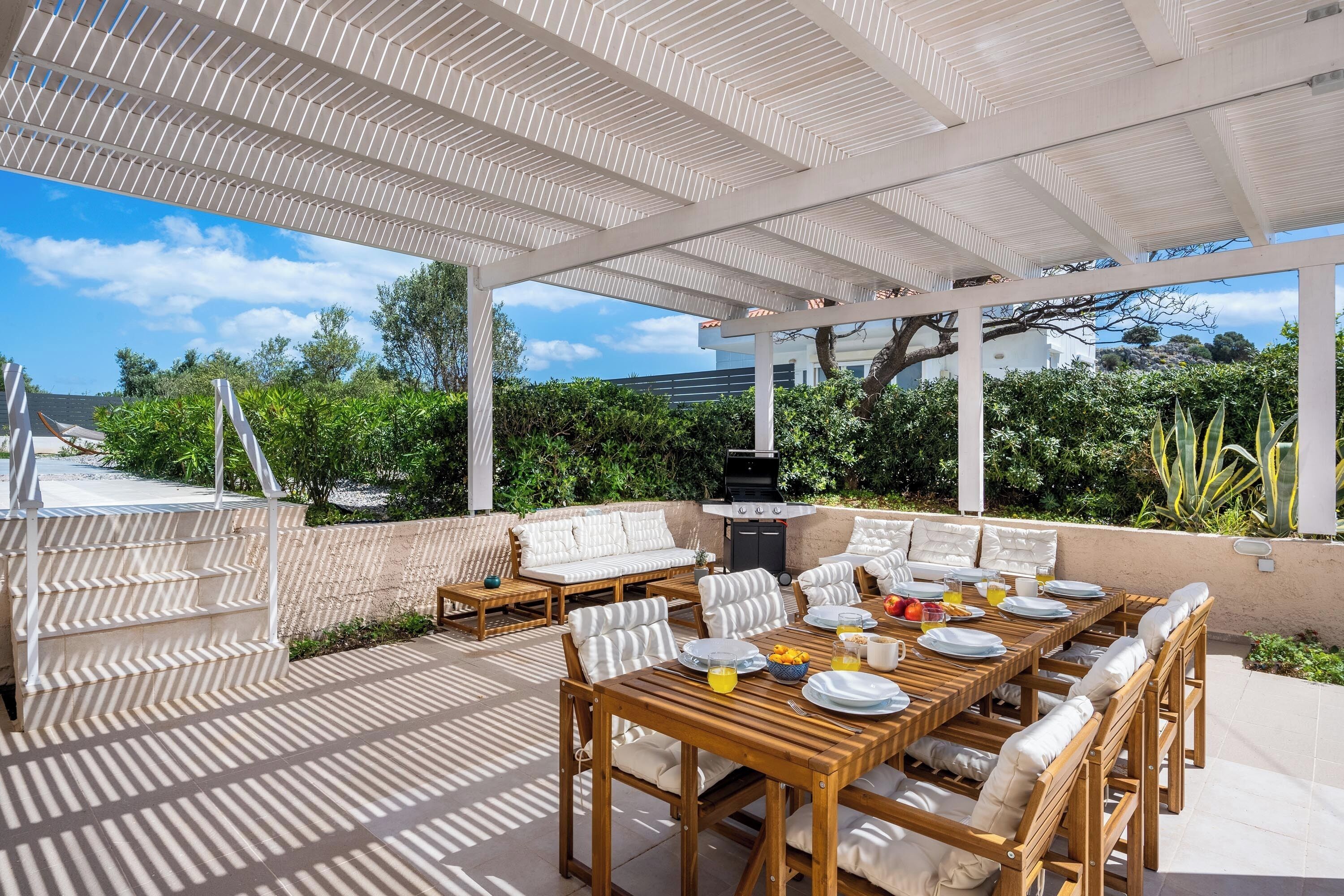 Eine Terrassenausstattung im Freien mit einem Holztisch, der zum Essen gedeckt ist, gepolsterten Sitzgelegenheiten und einem Grill.