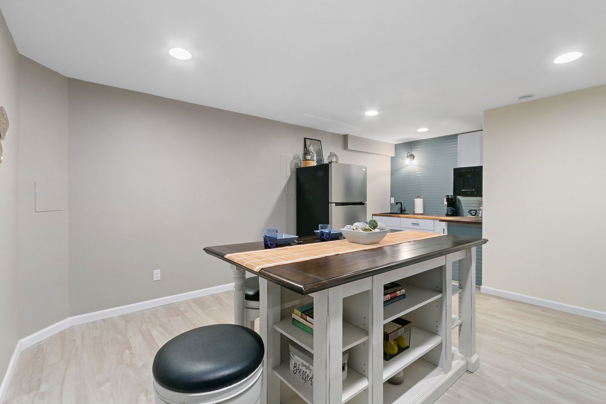 Una cocina moderna con una isla central, estantes empotrados y una zona de estar con un taburete acolchado negro.