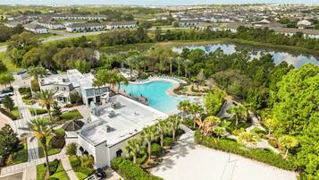An aerial view of a residential area with a swimming pool surrounded by greenery and a white sandy beach.