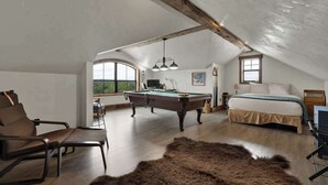 Une vaste chambre mansardée comprenant une table de billard, un lit et une grande fenêtre donnant sur l’extérieur.