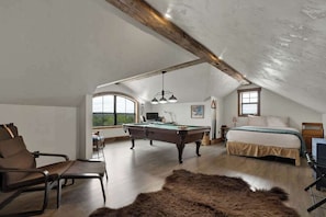 A spacious attic room with a pool table, a bed, and a large window offering a view of the outdoors. - West End Lodge Resort Style Pool (Fredericksburg)