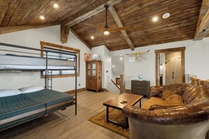 A rustic room with a bunk bed, a leather sofa, a wooden cabinet, and a ceiling fan. - West End Lodge Resort Style Pool (Fredericksburg)