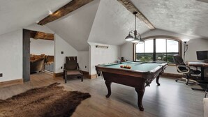Un loft spacieux avec une table de billard, une grande fenêtre offrant une vue dégagée et un plafond en bois rustique.