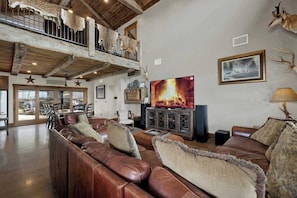 A spacious living room with a large leather sofa, a fireplace, and mounted animal heads on the wall. - West End Lodge Resort Style Pool (Fredericksburg)