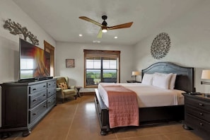 A bedroom with a bed, a ceiling fan, a dresser, a TV, a window, and a view of the outdoors. - West End Lodge Resort Style Pool (Fredericksburg)