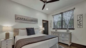 A bedroom with a bed, nightstands, a dresser, a ceiling fan, and a window with curtains. - West End Nest with Hot Tub (Fredericksburg)