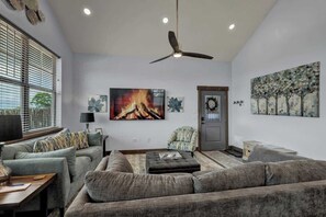 Ein modernes Wohnzimmer mit grauem Sofa, Kamin und Deckenventilator.
