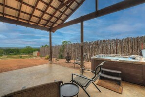 Un patio al aire libre con un jacuzzi, sillas y vistas al campo.