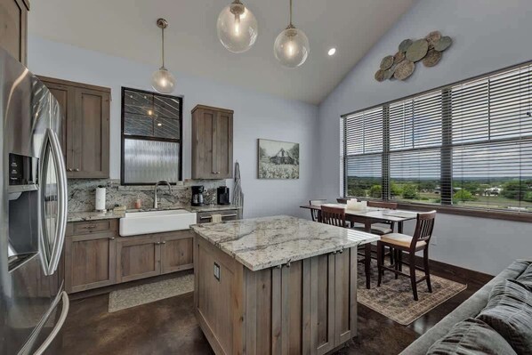 A modern kitchen with wooden cabinets, a marble island, and pendant lighting.