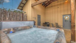 A hot tub in a wooden cabin with a rustic exterior, a door, and a small seating area. - West End Nest with Hot Tub (Fredericksburg)