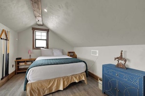 Een slaapkamer met een bed, een raam, een dressoir en een plafond met houten balken.