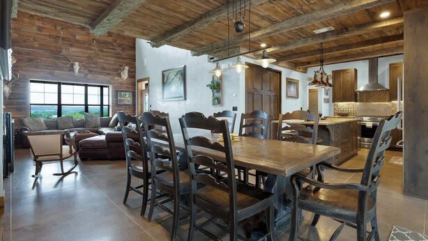 Amplia sala de estar con techo de madera, una mesa de comedor con sillas, un sofá y una cocina con armarios y un refrigerador.