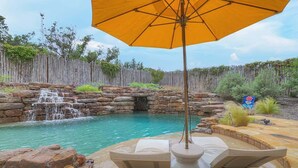 Un área de piscina con cascada, asientos de piedra y valla de madera.