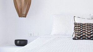 A neatly made bed with a white quilted bedspread and a single black pillow. - Cave Suite Paros, 65sq.m | Private pool & Panoramic sea view | "endless blue"
 (Paros Cyclades Greece)