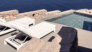 A pool with clear blue water, white lounge chairs, and a view of the sea. - Cave Suite Paros, 65sq.m | Private pool & Panoramic sea view | "endless blue"
 (Paros Cyclades Greece)