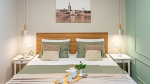 Ein ordentlich eingerichtetes Schlafzimmer mit einem Holzkopfteil, zwei Nachttischen mit Lampen, einem Bett mit einer grün-weißen Bettdecke und einem gerahmten Stadtbild an der Wand.