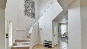 A clean, modern interior with a carpeted staircase, a wall-mounted abstract art piece, and a view into a living area with a sofa and coffee table.