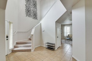 Um interior espaçoso com escadaria carpetada, parede branca com obra de arte geométrica e sala de estar com sofá e mesa de centro.