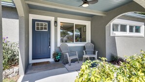 A house entrance with a dark blue door, two white windows, a ceiling fan, and a small porch area with two chairs and a table. - Tampa Home w/ Covered Patio: 8 Mi to Downtown! (Tampa)
