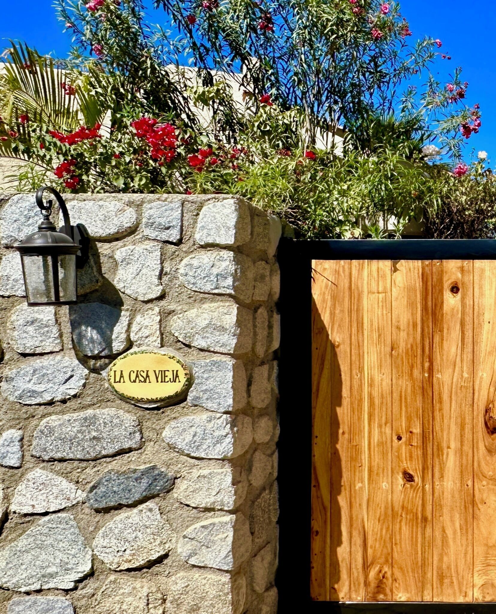 A stone wall with a sign reading "LA CASA VIEJA" and a wooden gate.