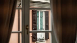 Vista a través de una ventana con contraventanas, un balcón y un tejado de tejas.