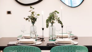 Mesa de comedor dispuesta con platos, vasos y velas, flanqueada por dos jarrones con plantas.