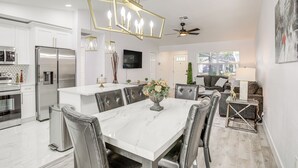 Une cuisine moderne avec des meubles blancs, un réfrigérateur en acier inoxydable et une table à manger en marbre, assortie de chaises en cuir.