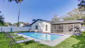 Un jardin avec une piscine, une terrasse couverte et une clôture blanche.