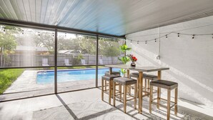 Un patio couvert avec vue sur la piscine, une table avec des chaises et des guirlandes lumineuses.