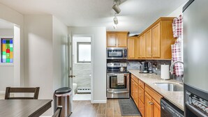 A modern kitchen with wooden cabinets, stainless steel appliances, and a dining area with a table and chairs. - Quaint Bristol Townhome ~ 14 Mi to West Hartford! (Bristol)