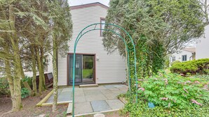 A residential garden with a stone patio, a green archway, and a variety of plants. - Quaint Bristol Townhome ~ 14 Mi to West Hartford! (Bristol)