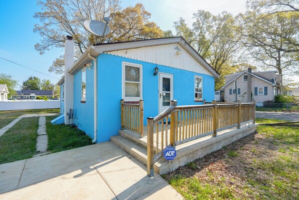 A single-story house with a blue exterior, a wooden front porch, and a satellite dish.