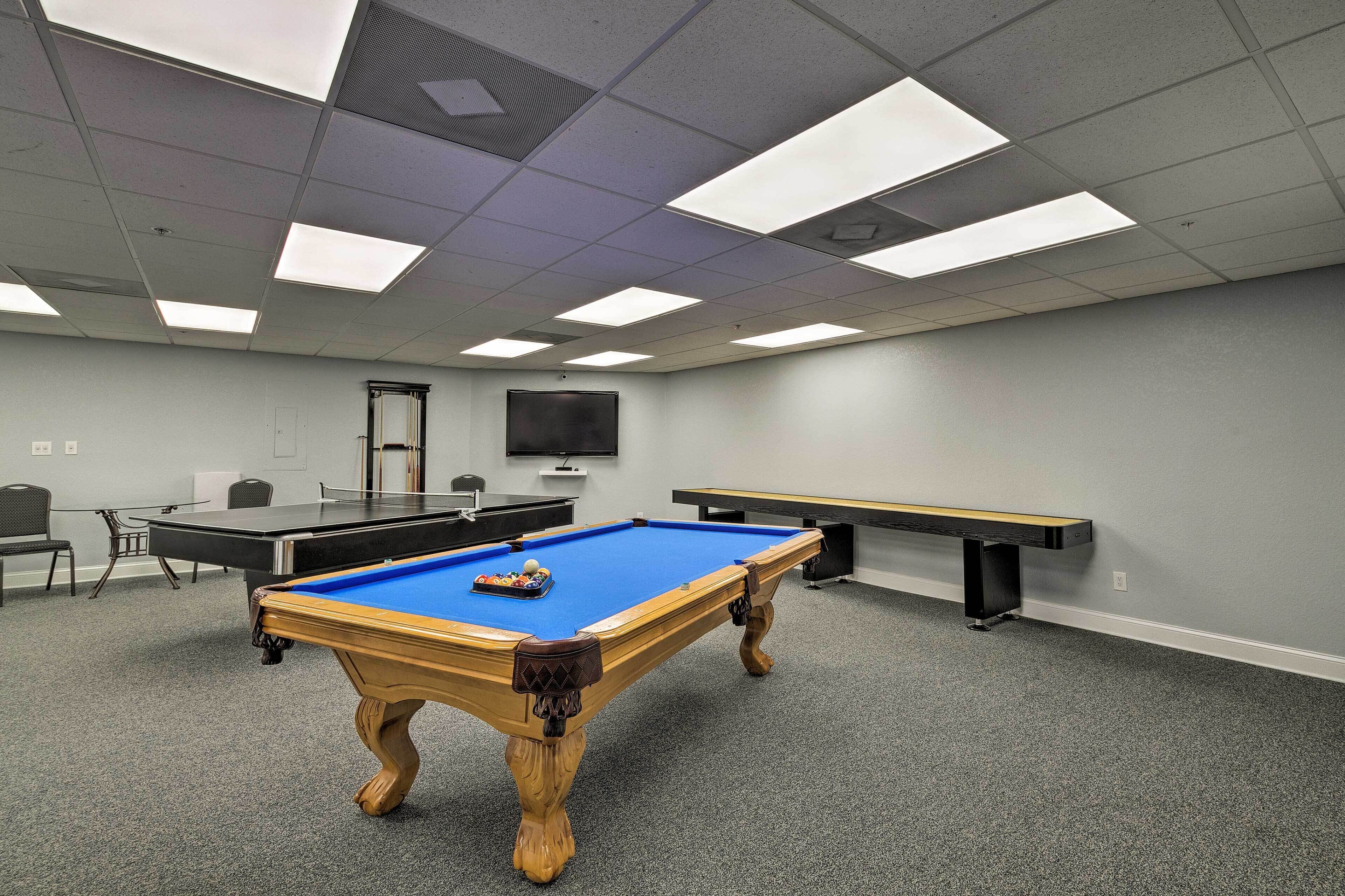 A room with a pool table, a billiards table, and a seating area with chairs.