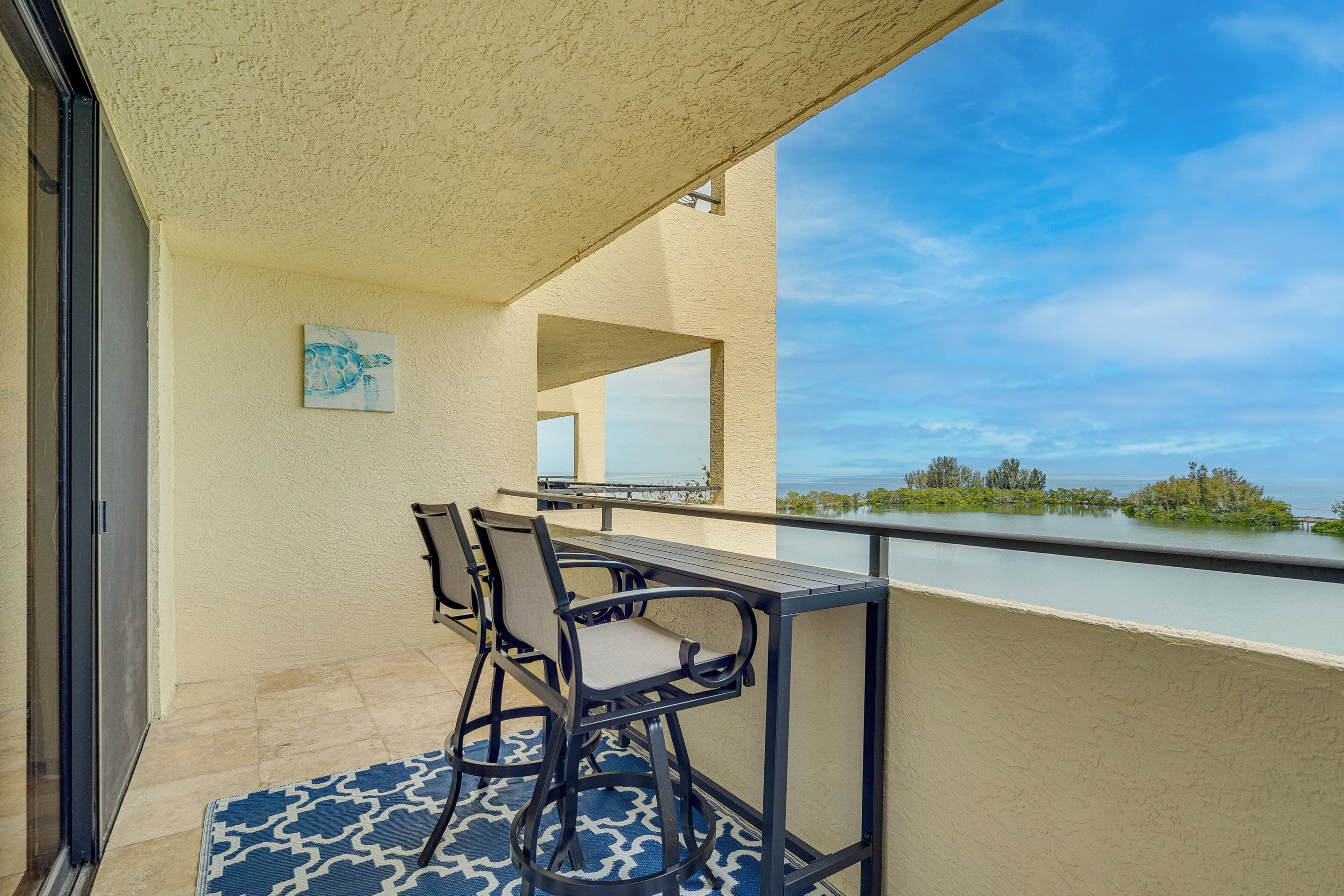 Un balcon avec une table et des chaises, une vue sur l’eau et un tableau accroché au mur.
