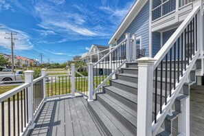 Une terrasse en bois avec une balustrade blanche menant à une maison à l’extérieur grise et dotée d’un escalier blanc.