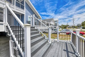 A wooden deck with a white railing, a staircase, and a view of a street with parked cars and houses.